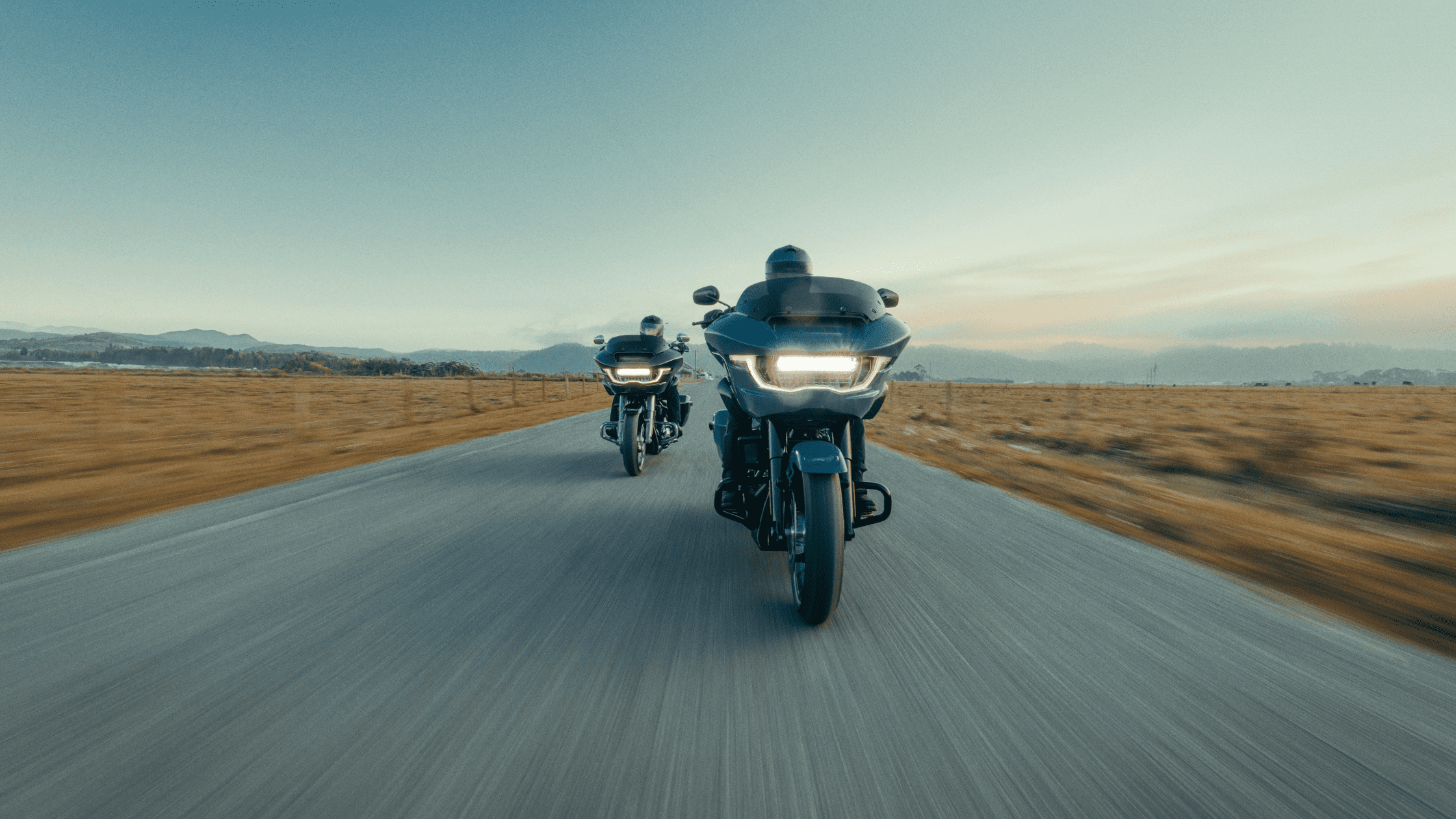 Two riders on the 2024 Harley-Davidson® Road Glide® models cruising along an open road near Covington, GA, highlighting the bike's touring capabilities and sleek design.