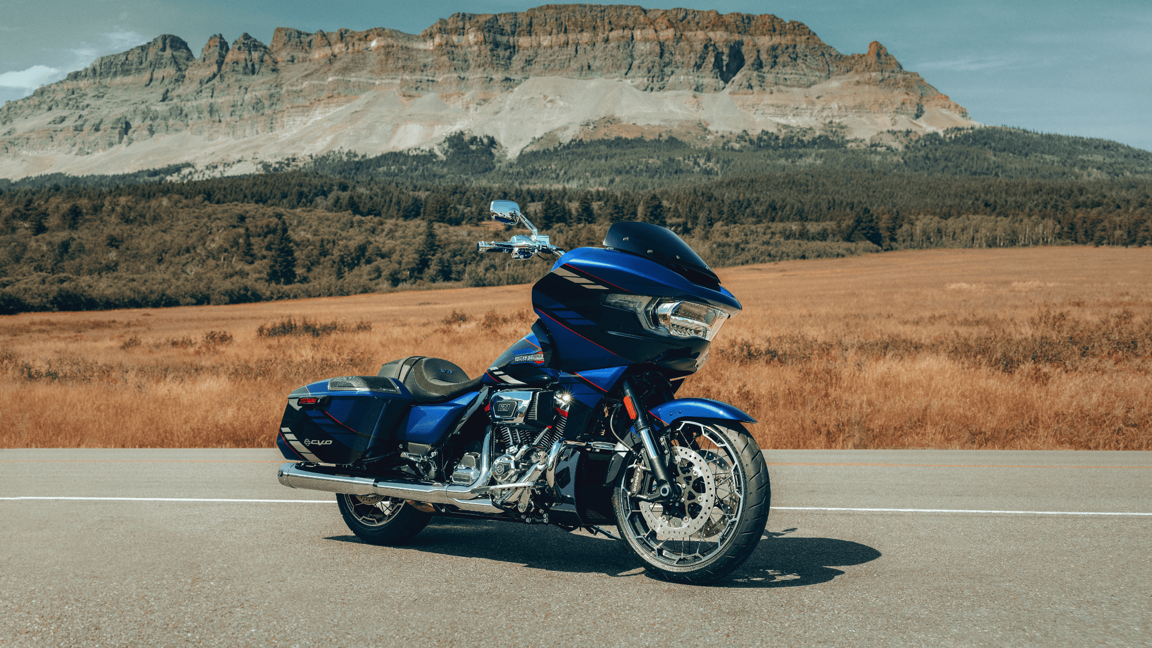 A blue CVO™ Road Glide® parked on an open road with a scenic mountain backdrop.